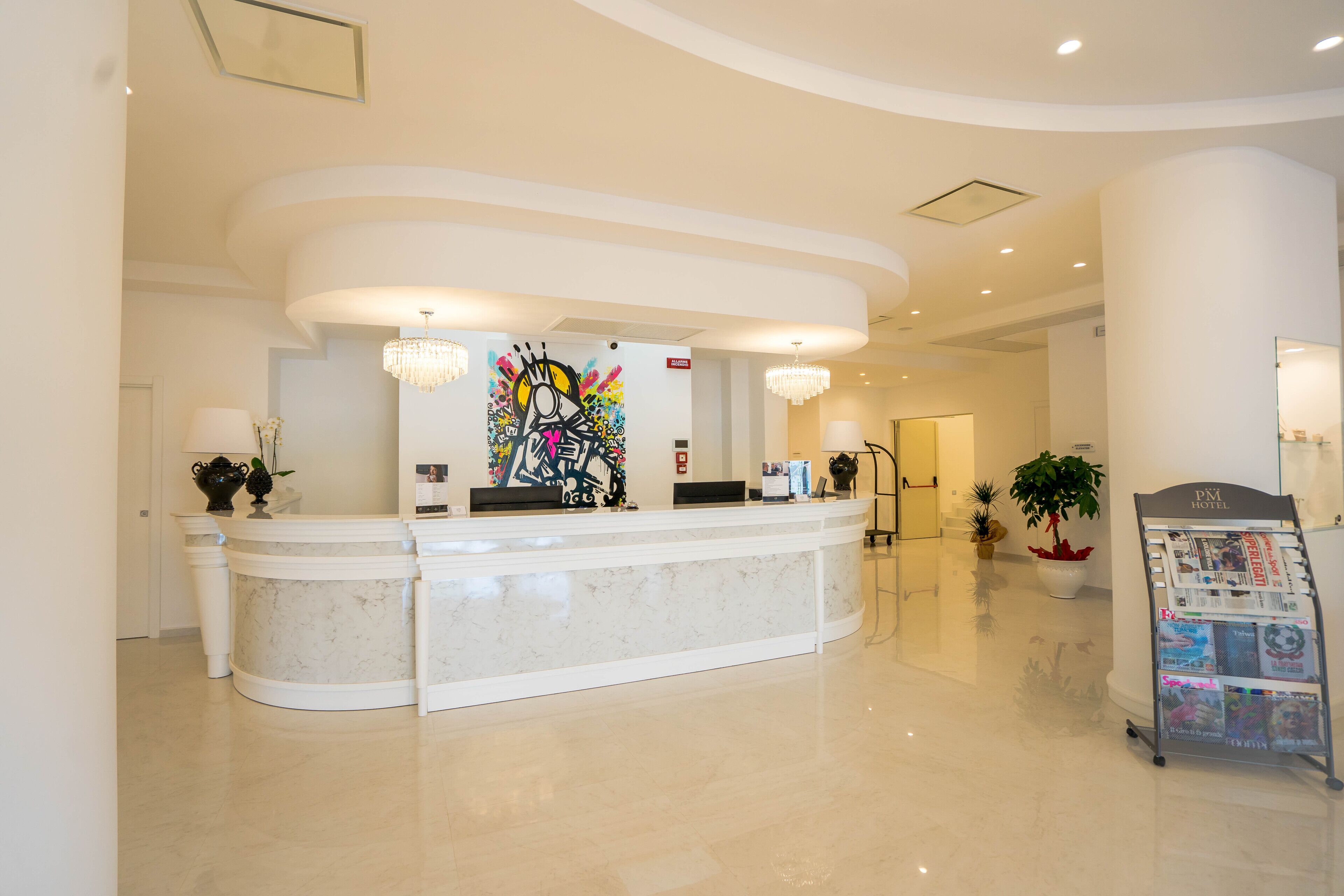 A hotel reception area with a marble counter, a colorful abstract painting, a chandelier, and a magazine rack.