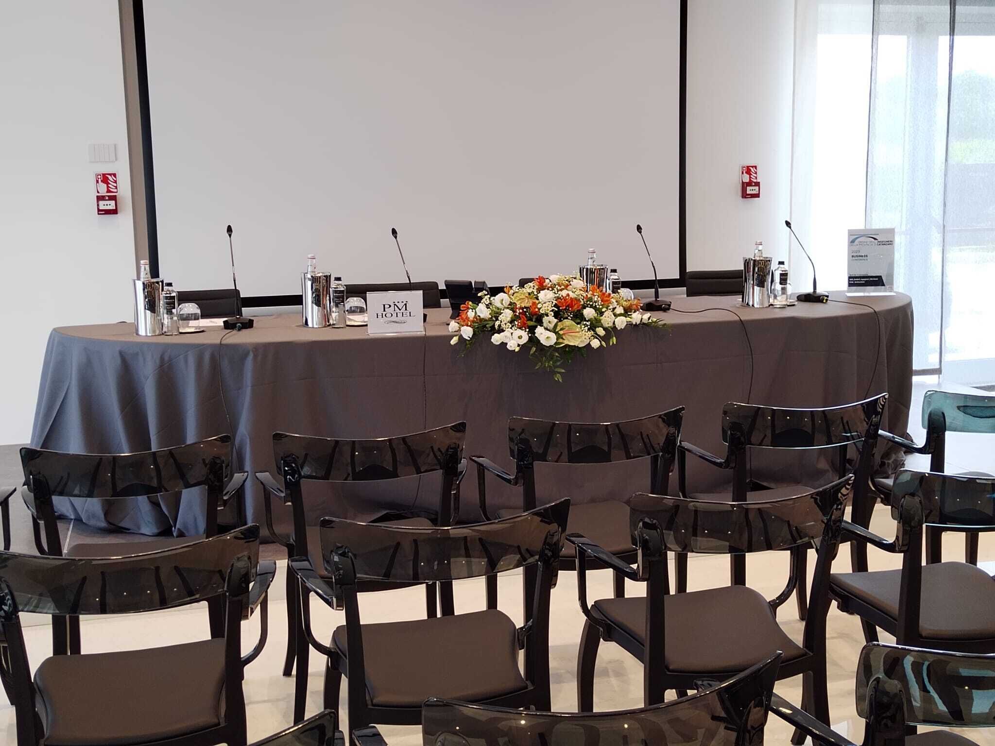 Une salle de conférence équipée d’une table ronde, de chaises, d’une plaque nominative, d’un microphone et d’un arrangement floral.