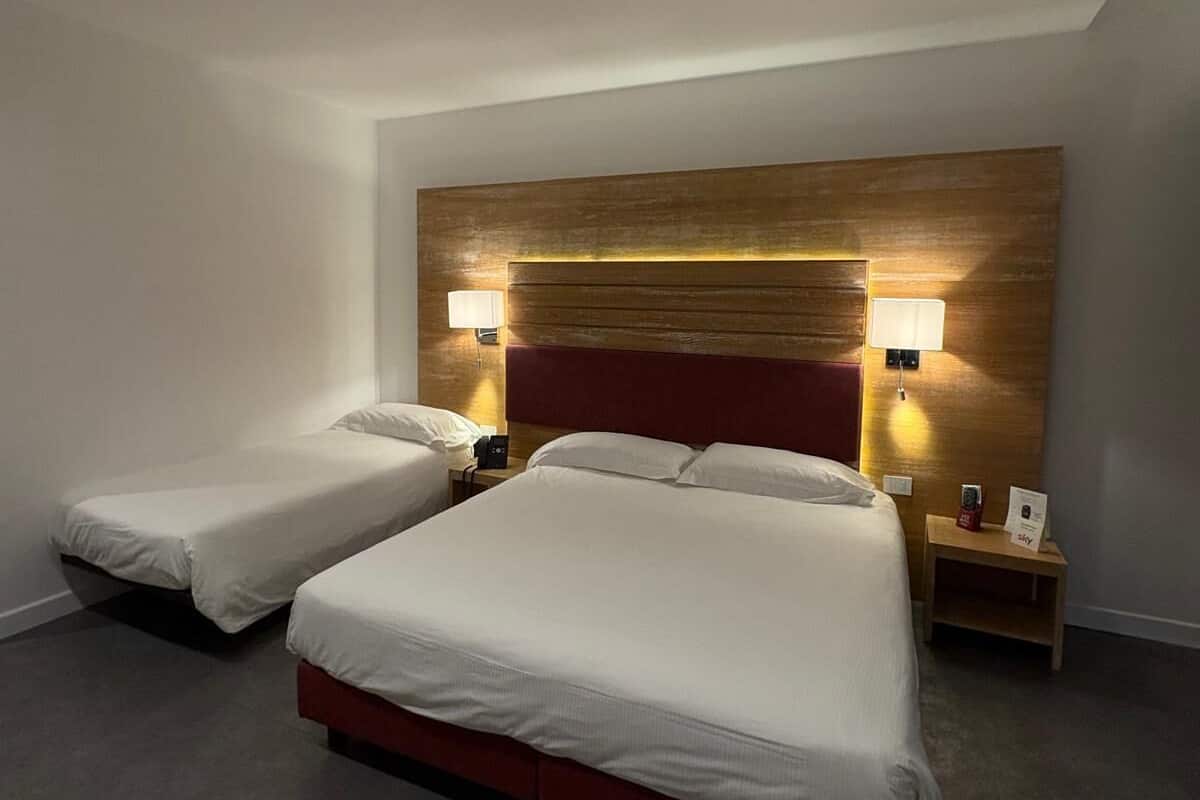 Ein Hotelzimmer mit zwei Einzelbetten, einem Holzkopfteil, Nachttischlampen und einem kleinen Tisch mit einer Uhr und einem Schild.