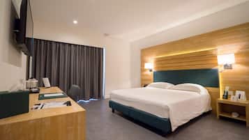 Una habitación de hotel con cama, escritorio, televisor, lámpara y mesita de noche.