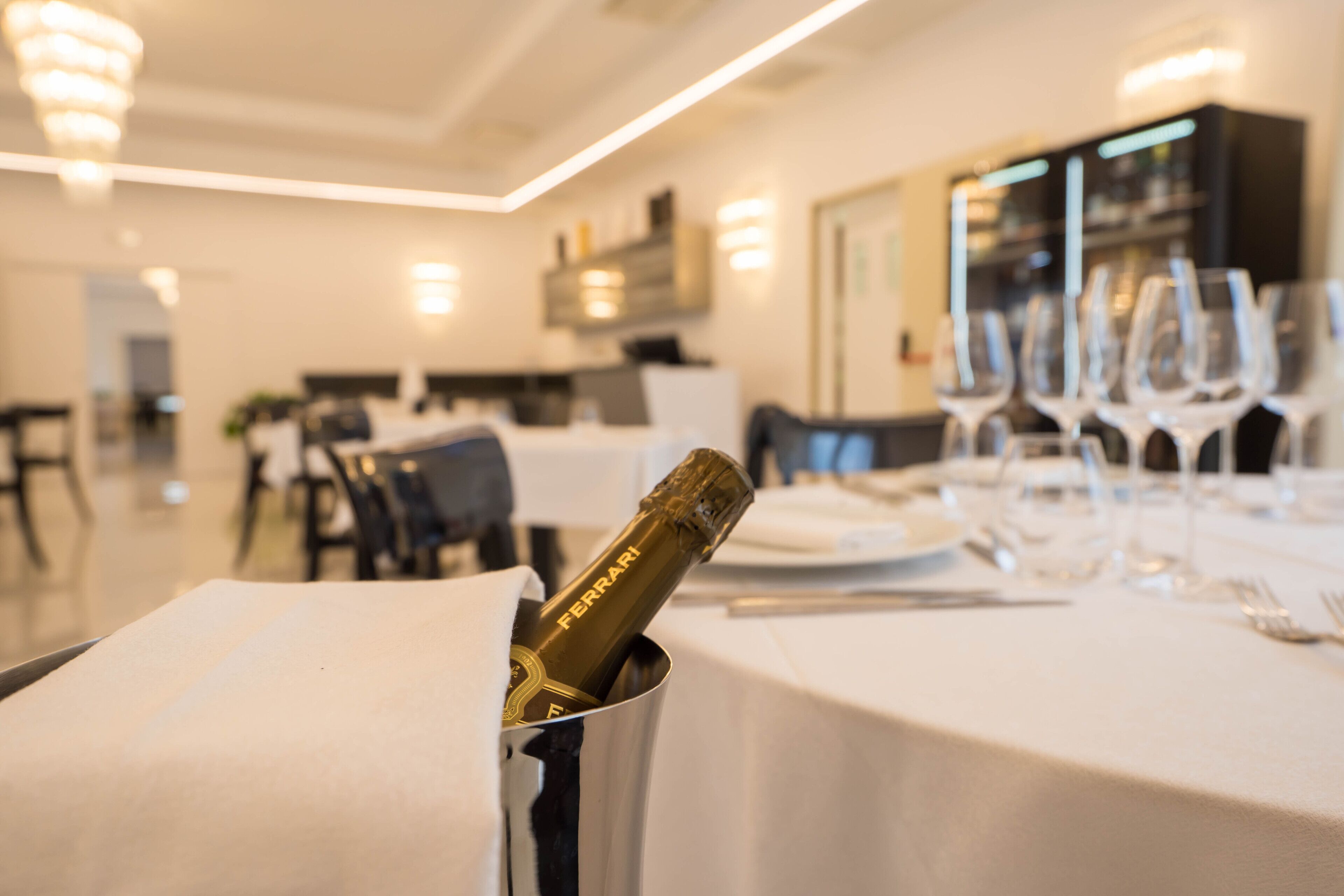 A dining area with a table set for a meal, a bottle of champagne in a holder, and a row of wine glasses.