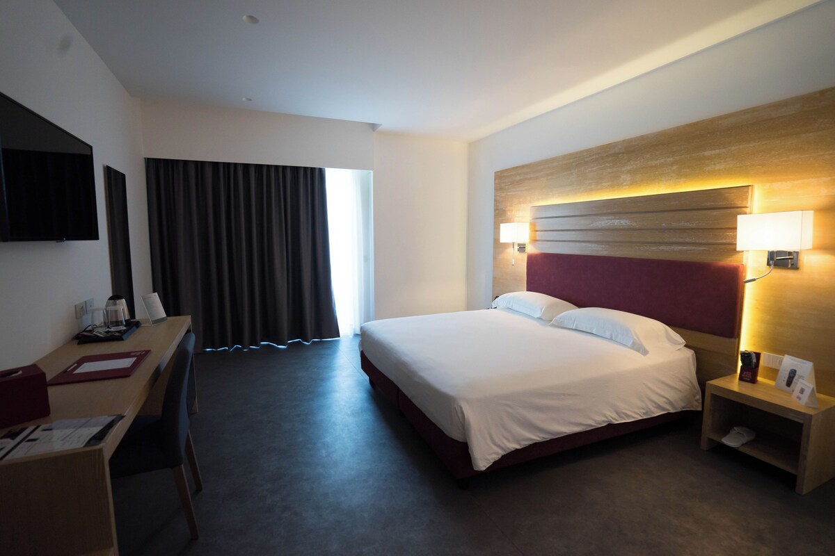 A hotel room with a bed, desk, and a TV mounted on the wall.