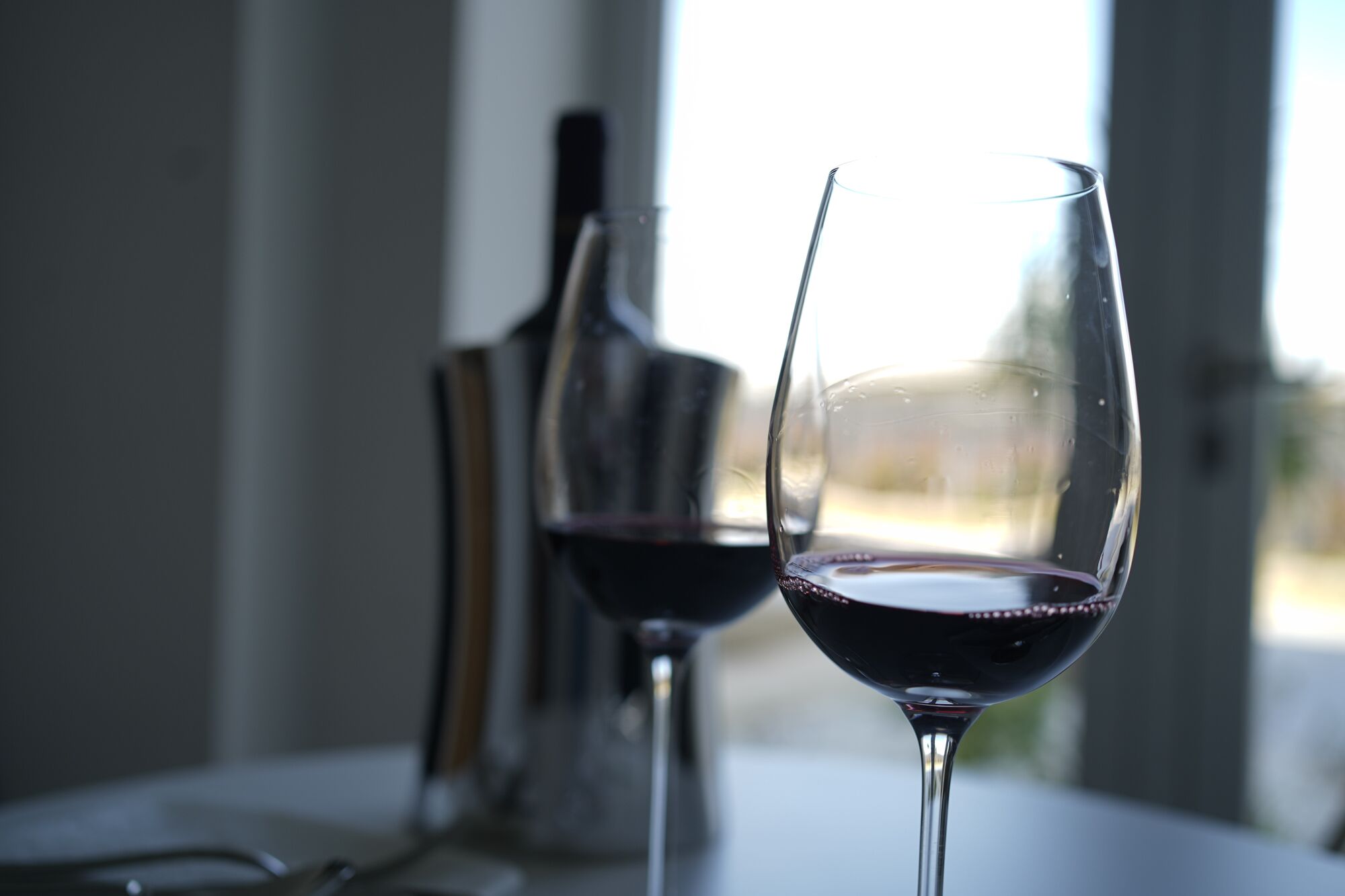 Two wine glasses on a table with a bottle in the background.