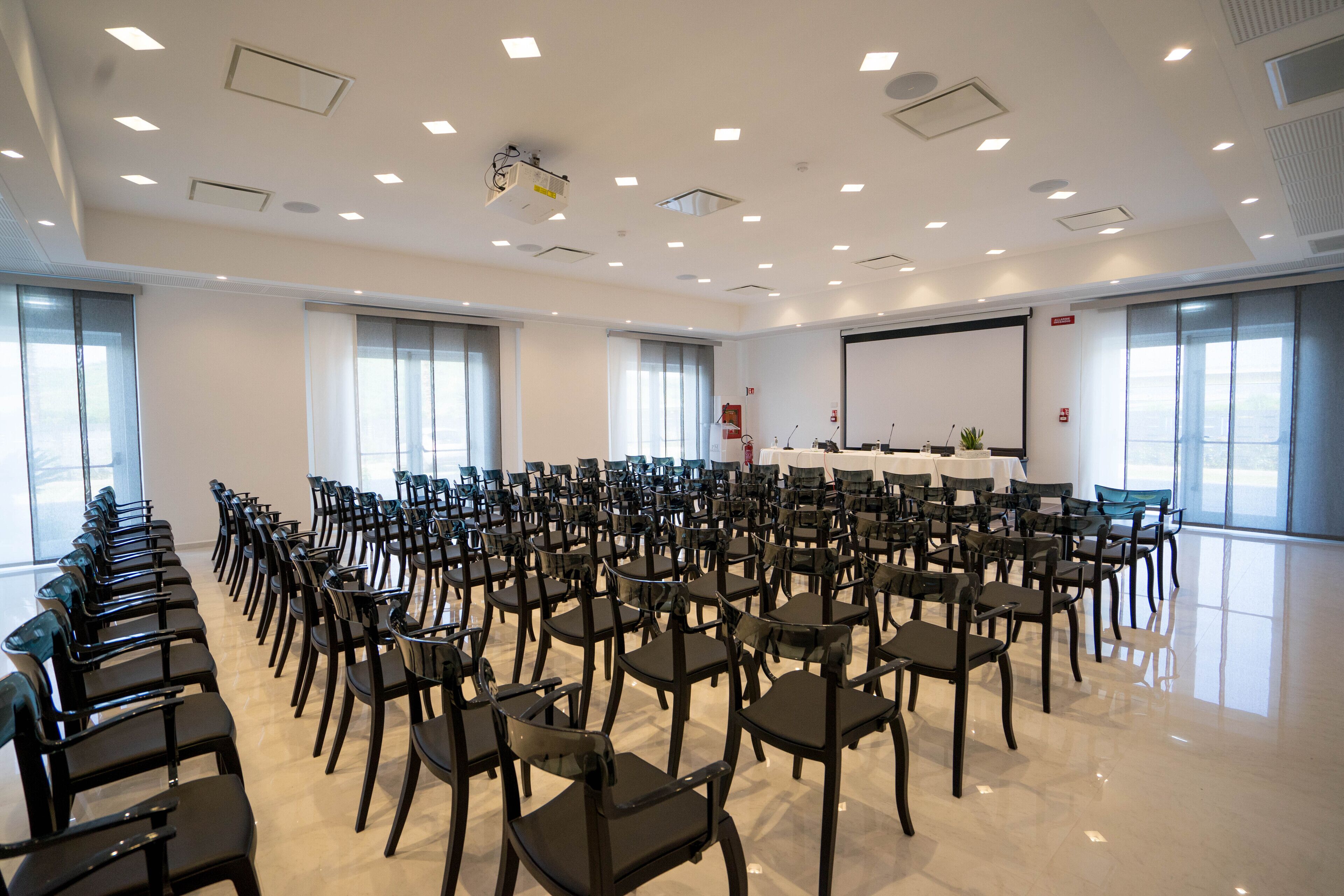 Une salle de conférence avec des rangées de chaises, un projecteur et un écran de présentation.
