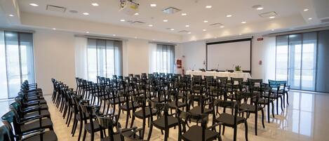 Uma sala de conferências com fileiras de cadeiras, um projetor e uma tela de apresentação.