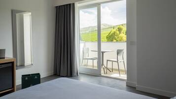 Hotelkamer met een groot bed, een bureau, een spiegel en een schuifdeur naar een balkon met stoelen en een tafel.