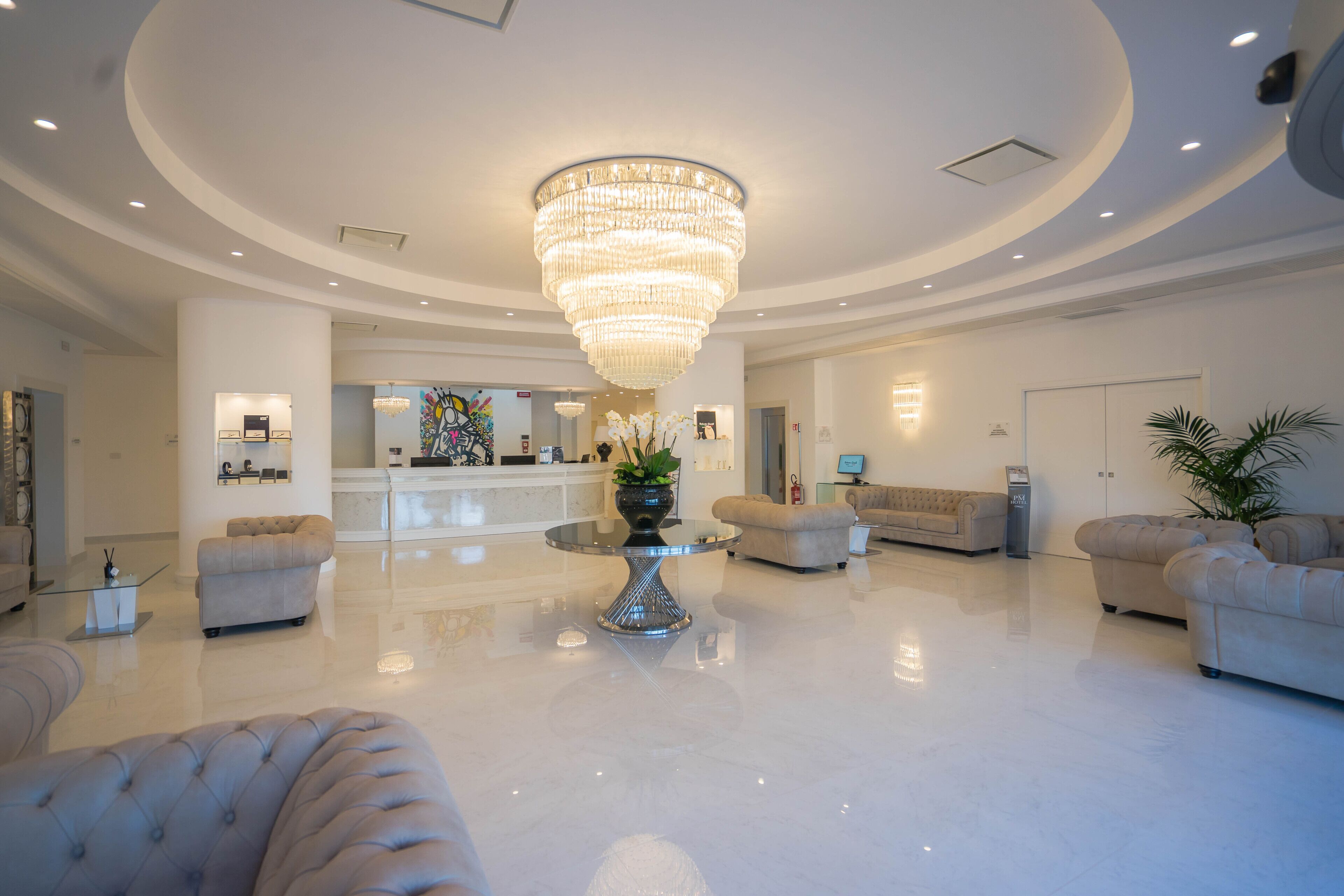 Un'ampia hall con un grande lampadario, comodi posti a sedere, una reception e un pavimento pulito e lucido.