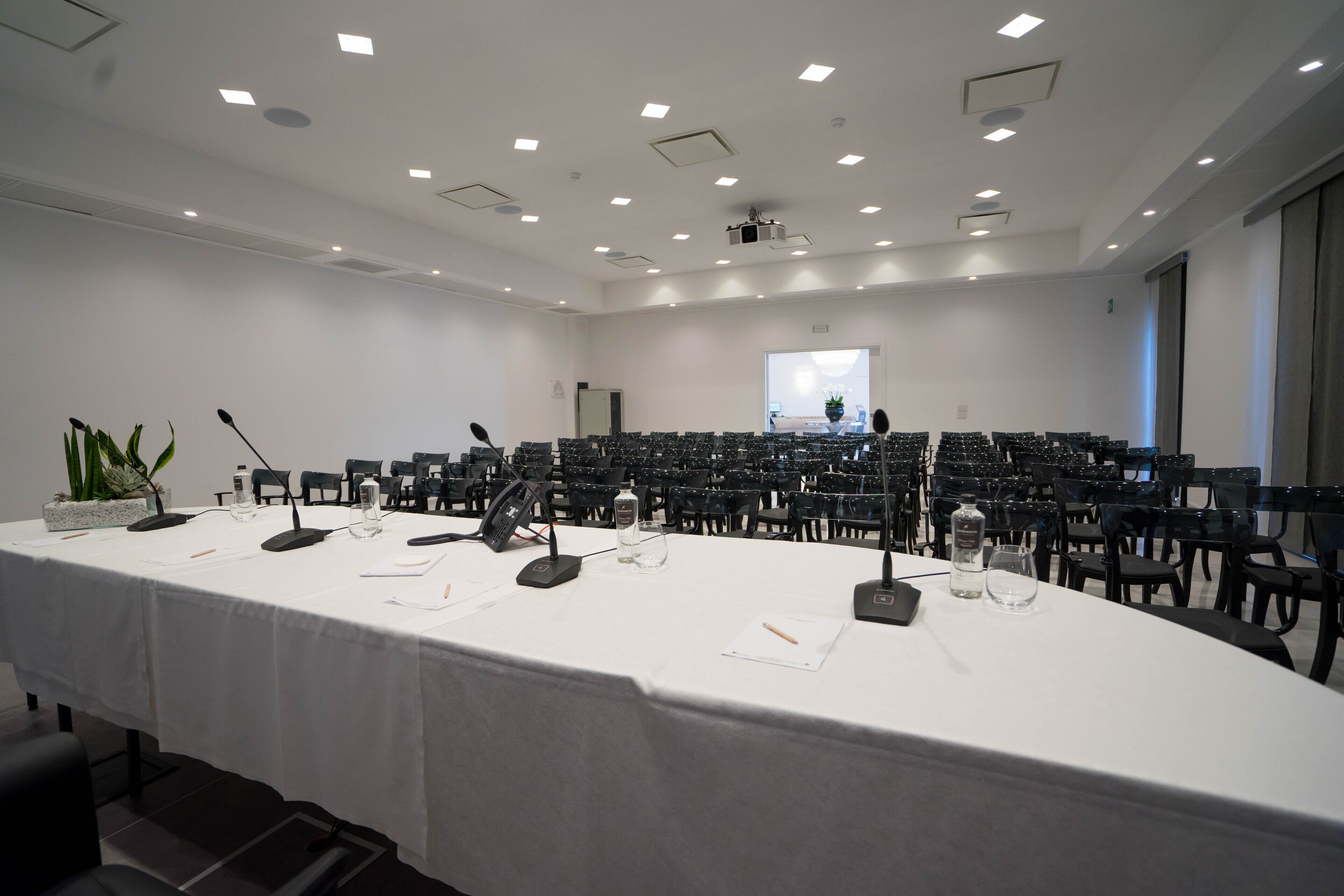A conference room with a long table, multiple chairs, microphones, and a projector screen.