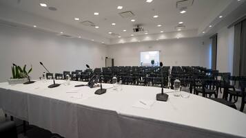 A conference room with a long table, multiple chairs, microphones, and a projector screen.