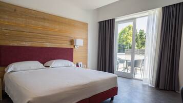 A hotel room with a large bed, a wooden headboard, a nightstand, a lamp, and a view of the outdoors through a sliding glass door.