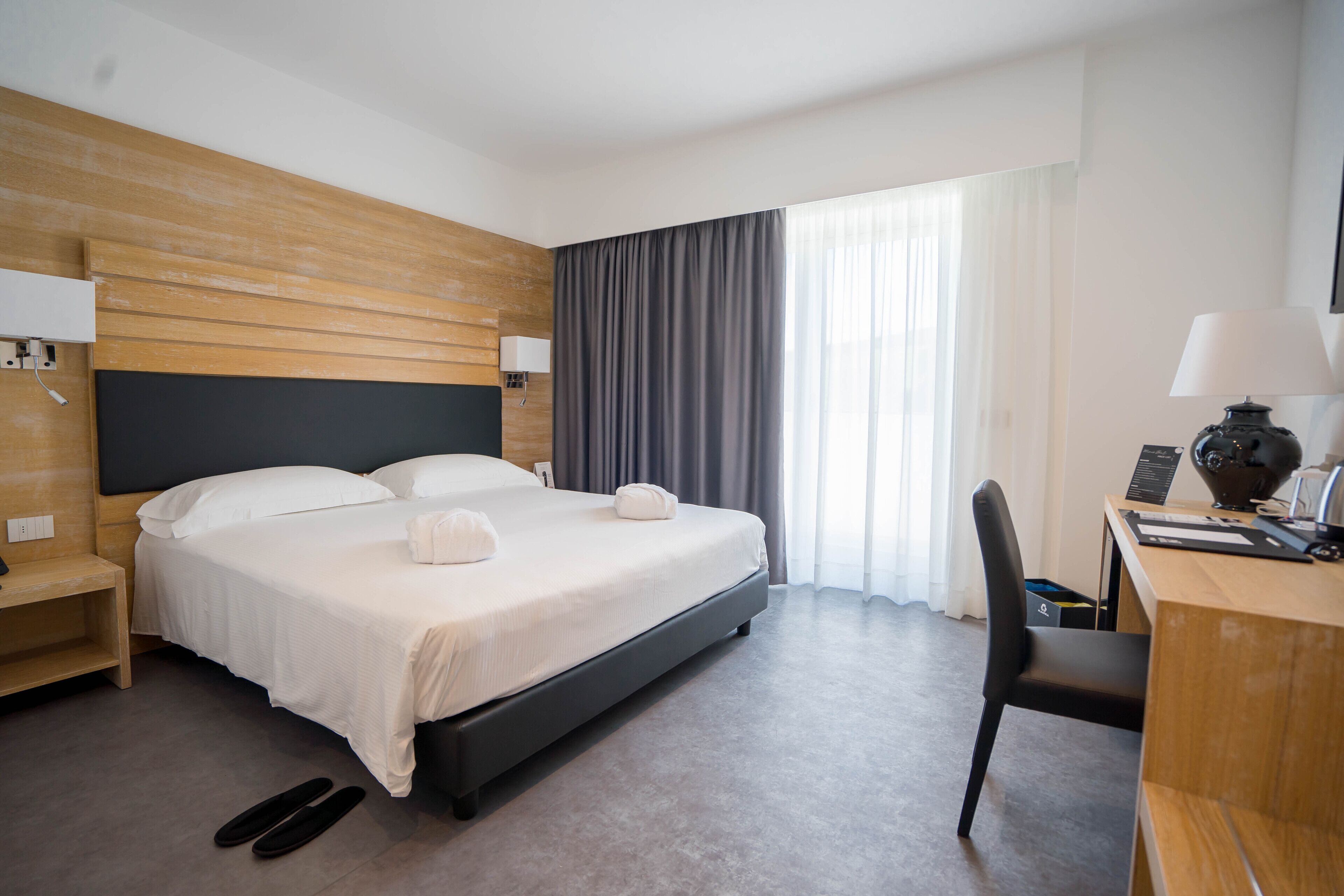 Een moderne hotelkamer met een groot bed, een bureau met een lamp en een stoel.