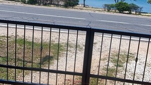 Un'area pavimentata con una recinzione in metallo sullo sfondo, un sentiero sterrato e un corso d'acqua con barche.