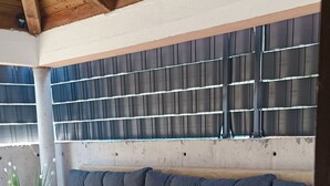 Un'area patio coperta con una zona salotto imbottita, una sedia bianca e una pianta in vaso.