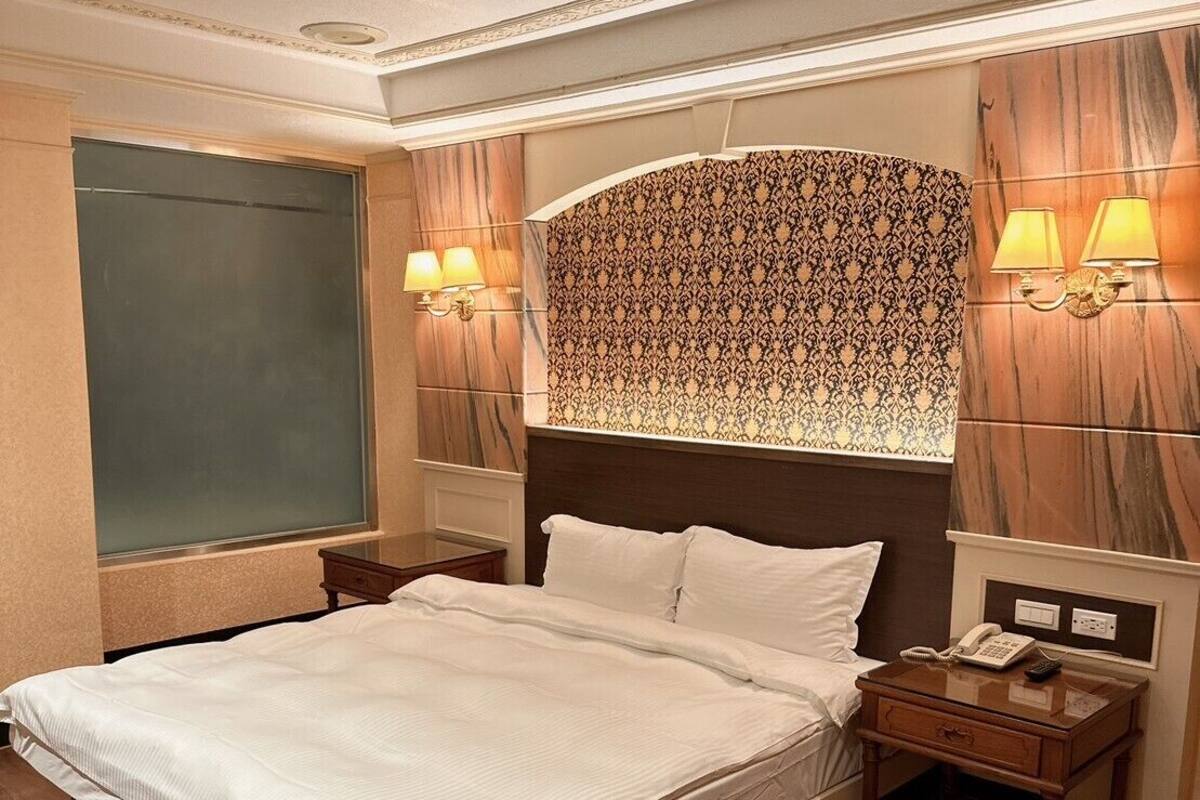 Ein Hotelzimmer mit einem großen Bett, zwei Nachttischen und einem verzierten Kopfteil.