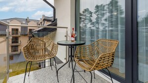 A balcony with two wicker chairs and a small table, a bottle of wine, and a view of neighboring buildings. - Climate Apartment | Balcony, Parking, 500 m to the Beach (Miedzywodzie)