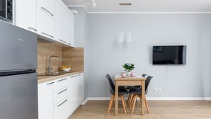 A modern kitchen with white cabinets, a stainless steel refrigerator, and a wooden countertop. There is a dining table with chairs and a potted plant. A flat-screen TV is mounted on the wall. - Climate Apartment | Balcony, Parking, 500 m to the Beach (Miedzywodzie)