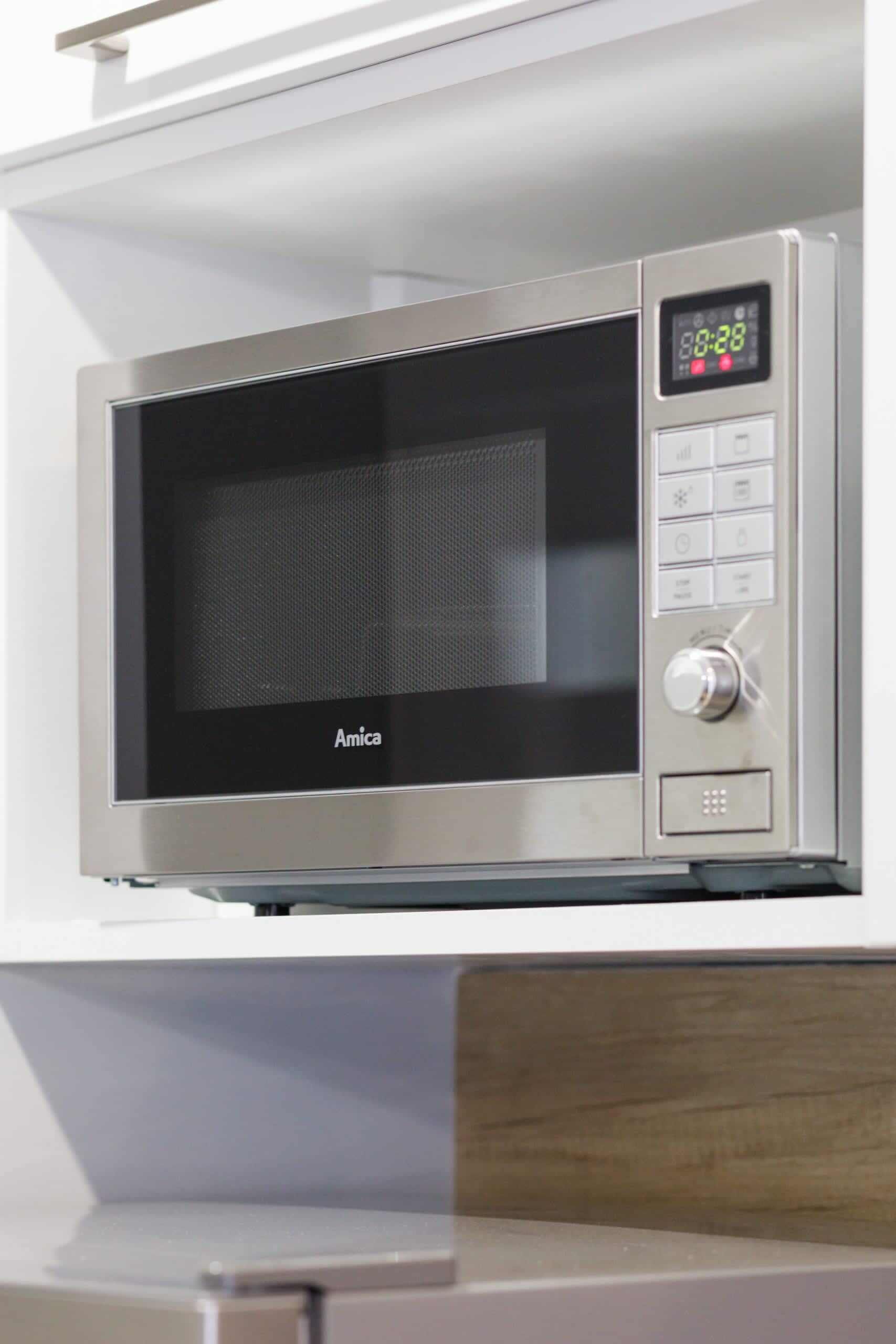 En mikrobølgeovn med digitalt display og kontrolpanel, placeret på en hvid hylde.