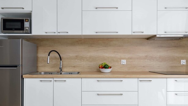 Una cucina moderna con mobili bianchi, elettrodomestici in acciaio inossidabile, un piano di lavoro in legno e una ciotola di frutta.