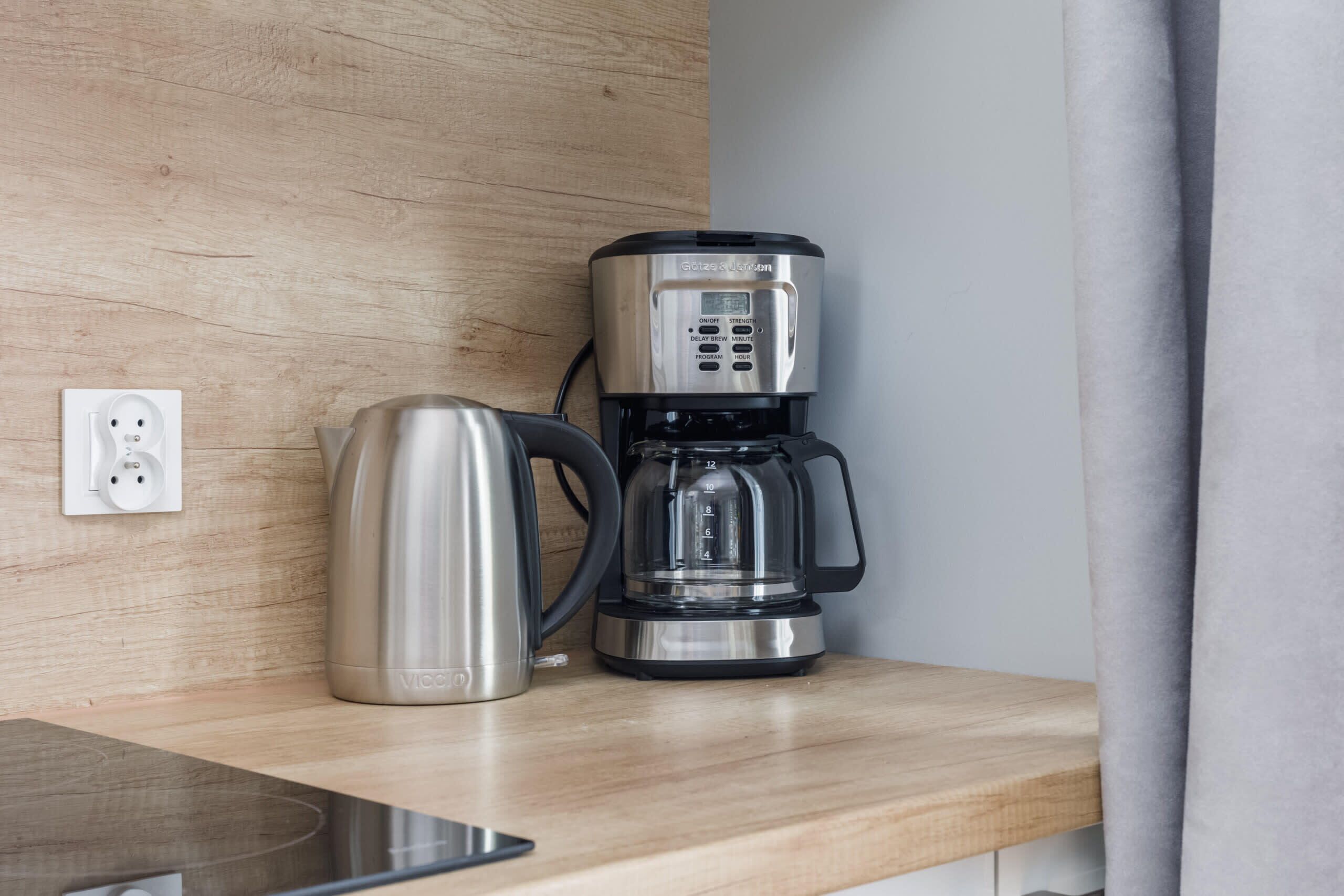 A modern kitchen with a stainless steel coffee maker and kettle on a wooden countertop.