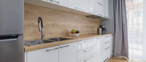 A modern kitchen with white cabinets, a wooden countertop, a stainless steel sink, and a coffee maker.