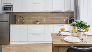 Una cucina moderna con mobili bianchi, un piano di lavoro in legno, un lavello, un forno a microonde e un'area pranzo con un tavolo apparecchiato per due, con piatti e bicchieri.