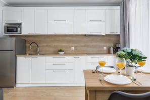 Una cocina moderna con armarios blancos, encimera de madera, un lavabo, microondas y un comedor con mesa dispuesta para dos personas, platos y vasos.