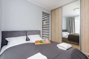 Een moderne hotelkamer met een groot bed, een houten garderobe, een spiegel en een dienblad met ontbijtartikelen.