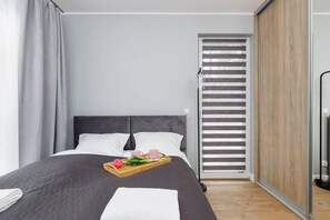 A modern bedroom with a large bed, grey curtains, a wooden side table with a tray of breakfast items, and a sliding glass door.