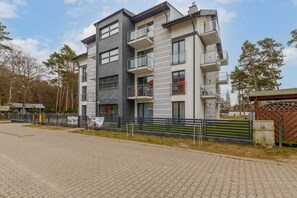 Un immeuble résidentiel à plusieurs étages, doté de balcons, d’une allée pavée et d’une entrée fermée par un portail.
