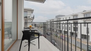 Un balcón con una mesa y una silla, con vista a una calle con edificios y coches estacionados.