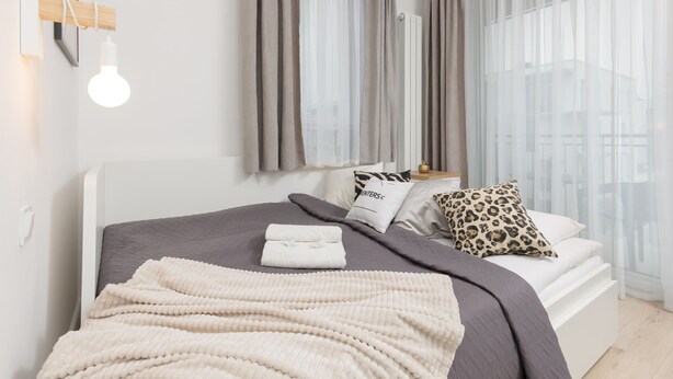 Un dormitorio moderno con una cama, una mesita de noche y un ventanal con cortinas translúcidas.