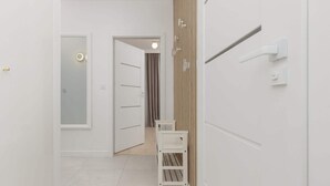 Un pasillo con paredes blancas, una puerta de madera y un banco blanco.