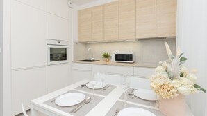 Una cocina moderna con armarios blancos, un microondas, un horno y una mesa de comedor preparada para cuatro personas, con platos, cubiertos y vasos blancos.