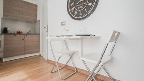 A compact kitchen with wooden cabinets, a white countertop, and a vintage clock on the wall.