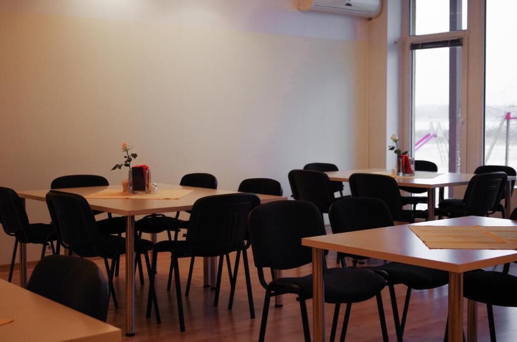 Un salón de conferencias con varias mesas y sillas, ventanas amplias y un equipo de aire acondicionado en la pared.