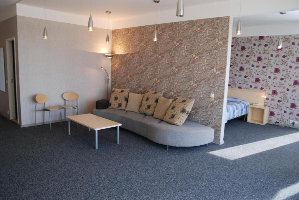 Een moderne kamer met een grijze bank, twee stoelen, een klein tafeltje en een bed met bloemenbehang.