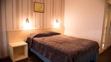 A hotel room with a bed, a nightstand, and a wall-mounted light fixture.