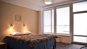 Un dormitorio con una cama, dos luces fijadas a la pared, un radiador y un ventanal con persianas.