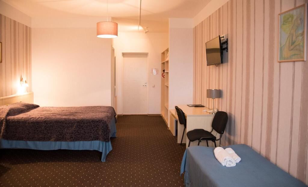 Una habitación de hotel con dos camas, un escritorio, una silla y un televisor en la pared.