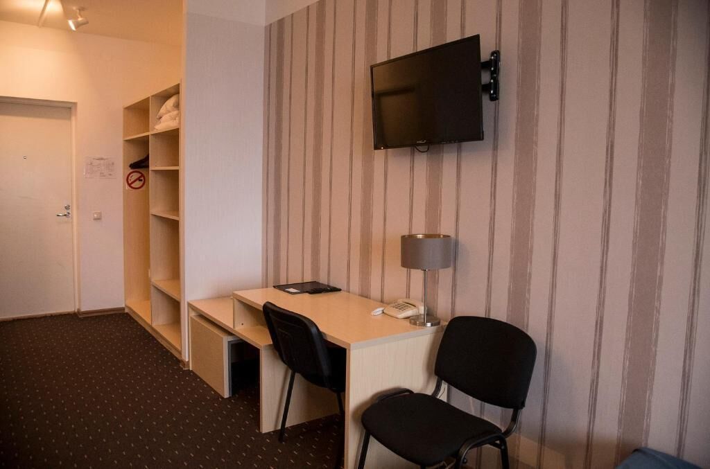 A hotel room with a desk, two chairs, a television mounted on the wall, a lamp, and a wardrobe.