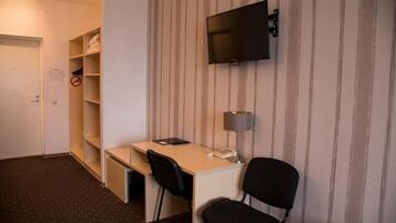 A hotel room with a desk, two chairs, a television mounted on the wall, a lamp, and a wardrobe.