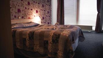 Ein ordentlich bezogenes Bett mit einer Steudecke, einer Nachttischlampe und einem floralen Wandpapier.