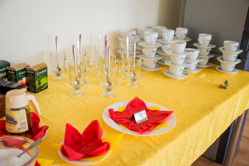 Una mesa de buffet con tazas y platillos blancos, vasos transparentes y servilletas rojas.