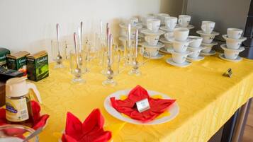 Una mesa de buffet con tazas y platillos blancos, vasos transparentes y servilletas rojas.