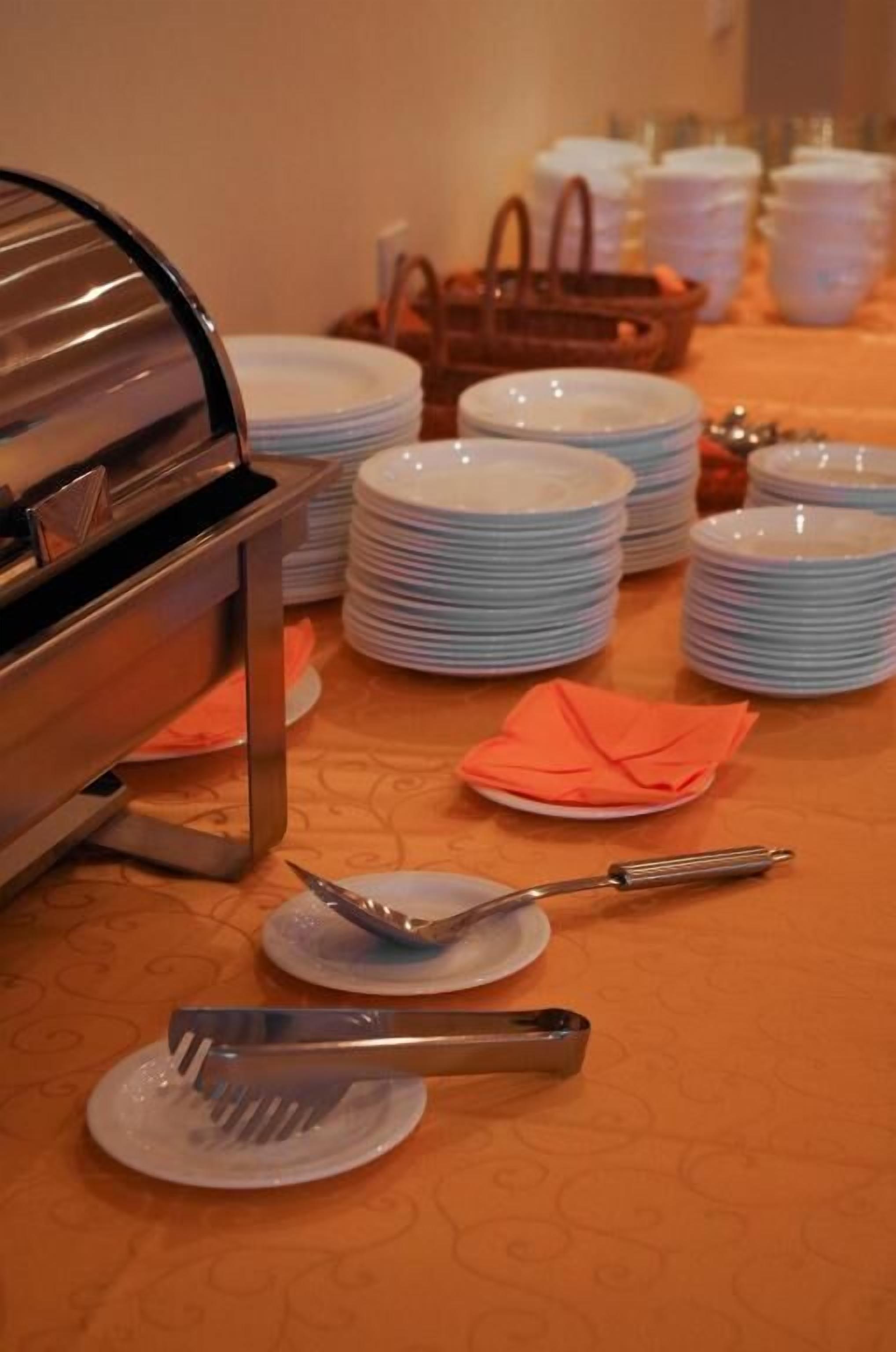 Un buffet est dressé avec des piles d’assiettes et de couverts sur une nappe à motifs.
