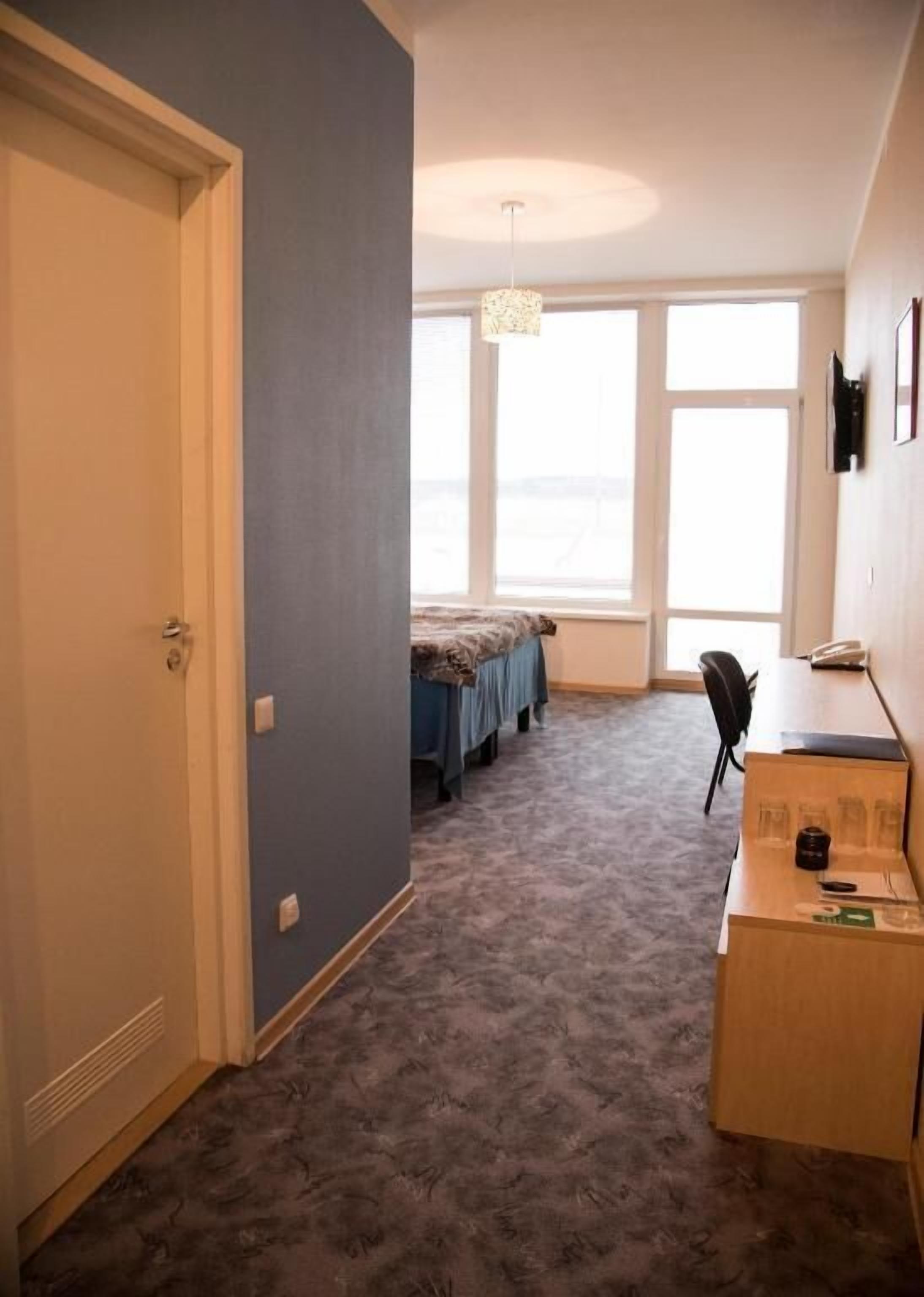 A room with a bed, a desk, and a chair. There are windows and a door.
