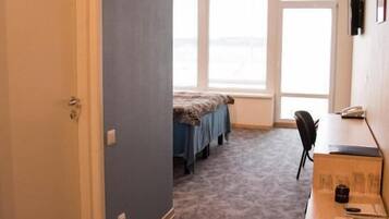 A room with a bed, a desk, and a chair. There are windows and a door.