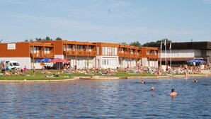Un hotel con varios pisos, piscina al aire libre y zona de playa con sombrillas.