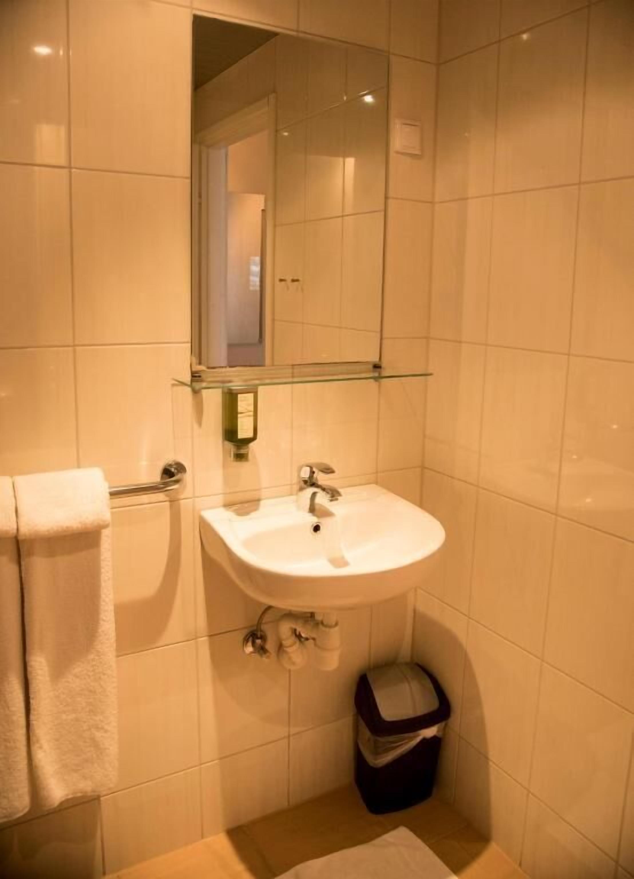 A bathroom with a white sink, a mirror, and a trash bin.