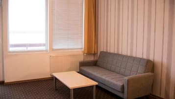 A small, sparsely furnished room with a sofa, a table, and a radiator.